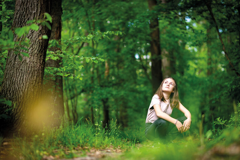 Junge Frau sitz im Wald auf dem Boden und blickt in die Baumwipfel