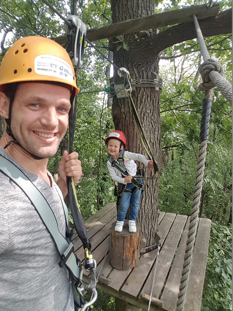 Man mit Helm und Klettergurt und Kind in den Baumwipfeln